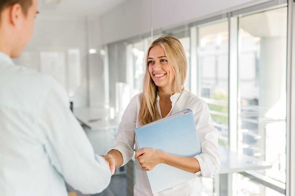 A young female med student smiling and shaking hands with a doctor in a hospital corridor.